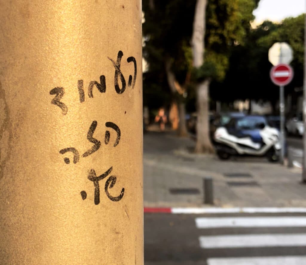 עמוד חשמל ברחוב תל אביבי עליו כתוב עם טוש: ״העמוד הזה שלי״. רקע מטושטש של מעבר חציה ואופנוע לבן חונה